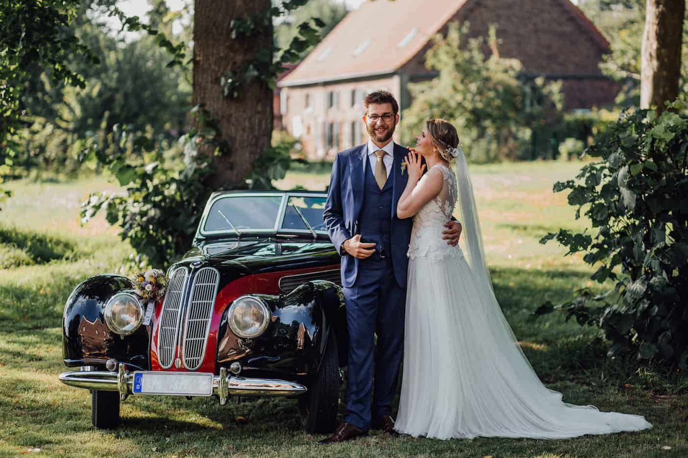 Hochzeit von Laura und Marco in Münster: Brautpaar steht vor einem historischen Auto